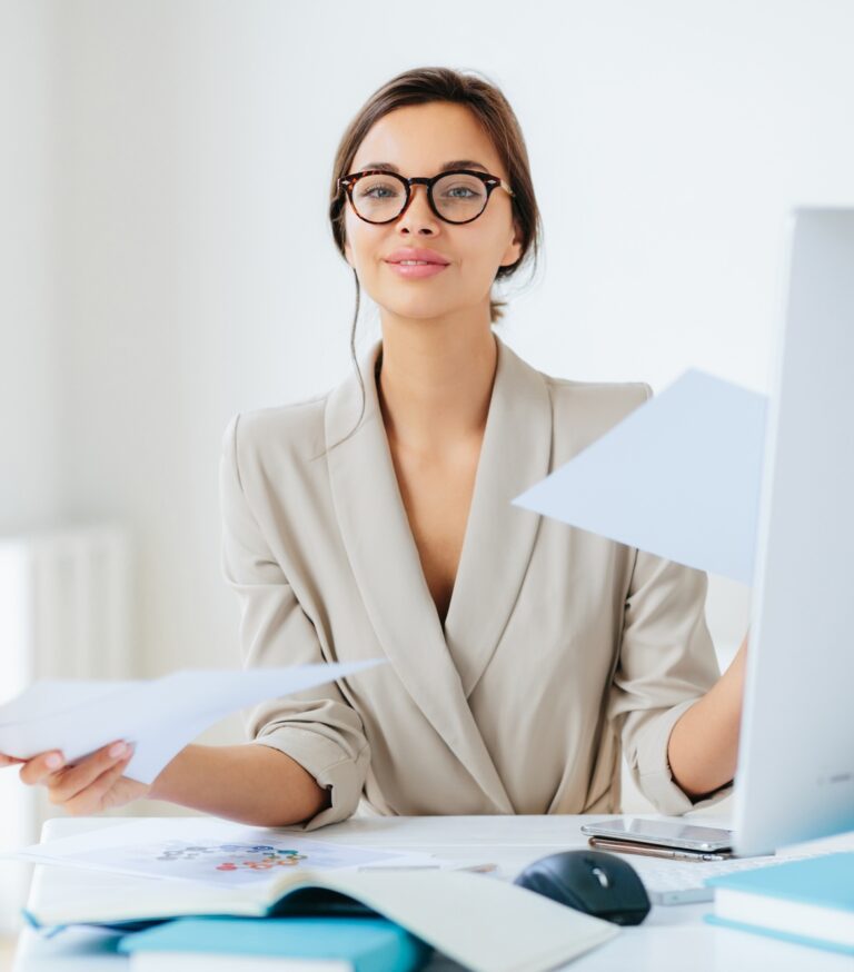 Busy successful female manager works with papers in office, poses at desktop
